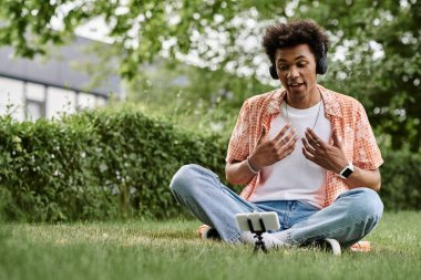 A young man sitting on grass, immersed in music.