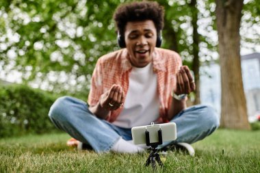 Young African American man sitting on grass, engrossed in cell phone.