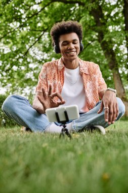 Young man immersed in music sits on grass in park with headphones on.