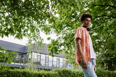 Young man of African American descent standing in park near building.