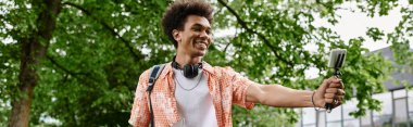 Young man, African American, holding a microphone in a park.