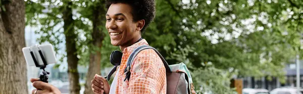 stock image Young African American man, backpack on, using cell phone in the park.
