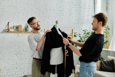 İki adam, tasarımcılar, yaratıcı bir atölyede birlikte, moda kıyafetleri üzerinde çalışıyorlar..