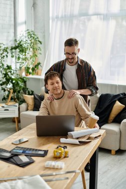 men sits at a table, focused on his laptop as he collaborates on creating fashionable attire. clipart