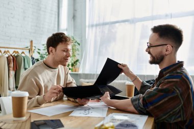 A gay couple works together in a designer workshop, crafting trendy attire. clipart