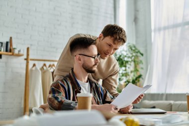 Two men in a workshop, engrossed in designing fashion pieces on a table. clipart