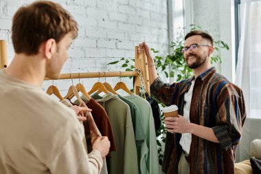 A man stands confidently in front of a rack of colorful, trendy clothes, showcasing his creative talent and dedication to fashion design. clipart