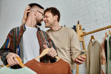 Two men, members of a gay couple, stand side by side in a designer workshop. clipart