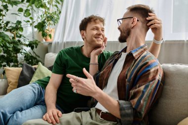 Two men, a gay couple, sit on a couch in a designer workshop, passionately discussing and creating trendy attire. clipart