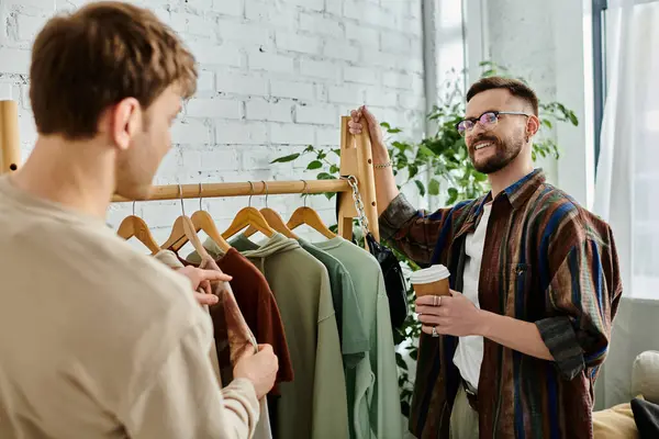 stock image A man stands confidently in front of a rack of colorful, trendy clothes, showcasing his creative talent and dedication to fashion design.