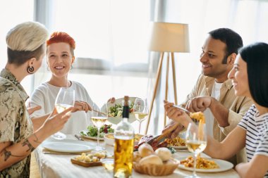 A diverse group of friends enjoy a meal together at a dinner table hosted by a loving lesbian couple. clipart