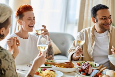 Çeşitli bir arkadaş grubu yemek ve içeceklerle dolu bir masada birlikte yemek yiyor..
