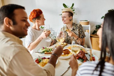 Çeşitli gruplar yemeğin tadını çıkarıyor, merkezde lezbiyen çift var..