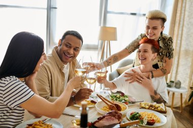 Çeşitli bir grup yemek masasının etrafında oturuyor. Aralarında sevecen bir lezbiyen çift ve arkadaşları da var..