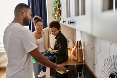 Bir adam ve bir kadın oğluyla birlikte bir mutfak temizliyor ve düzenliyorlar..