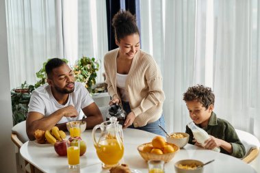 Parents and boy sitting at table with pitcher of orange juice. clipart