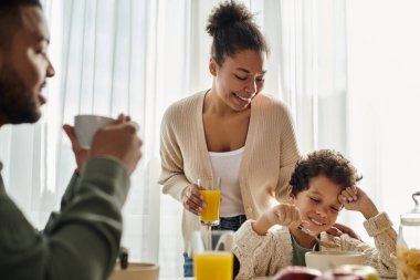 Bir kadın, önünde bir çocuk ve bir kocayla masada oturuyor..