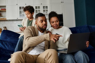 Afro-Amerikan ailesi bir kanepede otururken dizüstü bilgisayar kullanıyor..