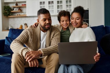 Man, woman, and child watch laptop on couch. clipart