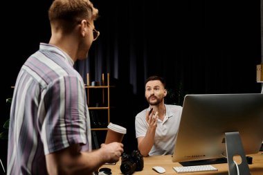 Günlük kıyafetli iki adam, ofiste bir masaüstü bilgisayarının önünde tartışıyorlar..