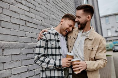 Two men in casual attire standing together by a brick wall. clipart