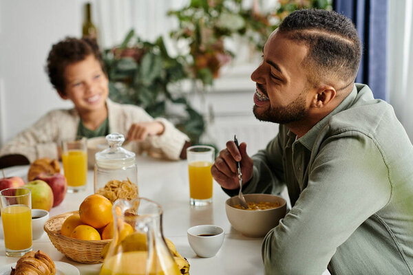 Men at table eating food next to his son.