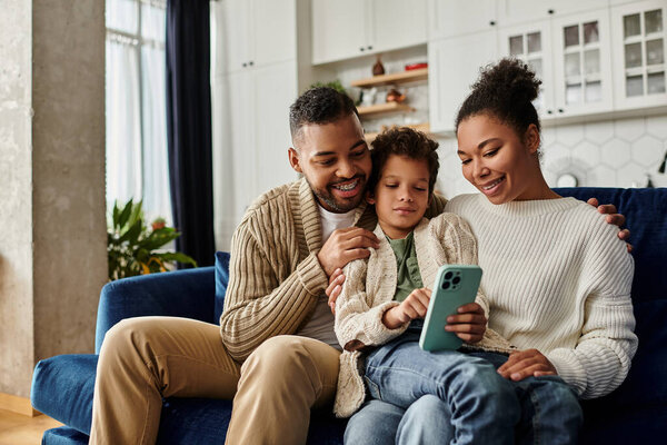 Man, woman, and child on couch engrossed in cell phone.