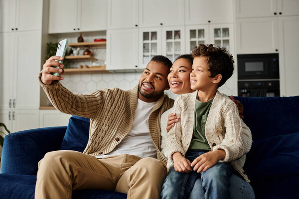 Афроамериканец делает селфи со своей женой и ребенком на диване.