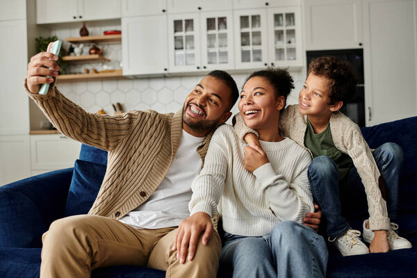 Афроамериканская семья счастливо сидит на диване, делая селфи вместе.