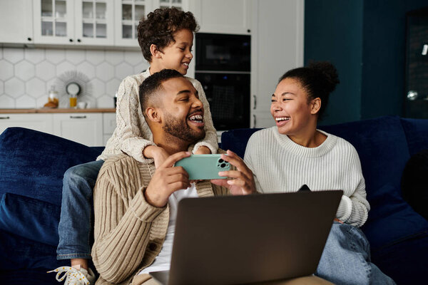African american family focus on laptop screen while sitting on a couch.