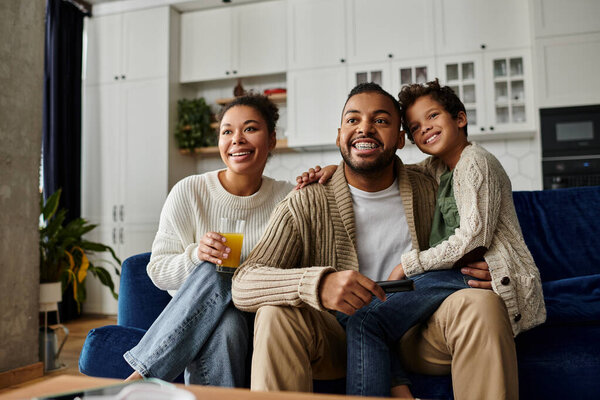 Афроамериканец, женщина и ребенок сидят вместе на уютном диване в гостиной.