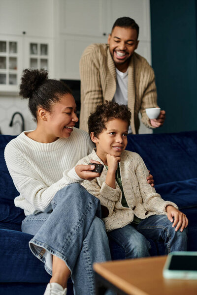 Мужчина и женщина, афроамериканец, сидят вместе на синем диване, показывая любовь и единение, с сыном.