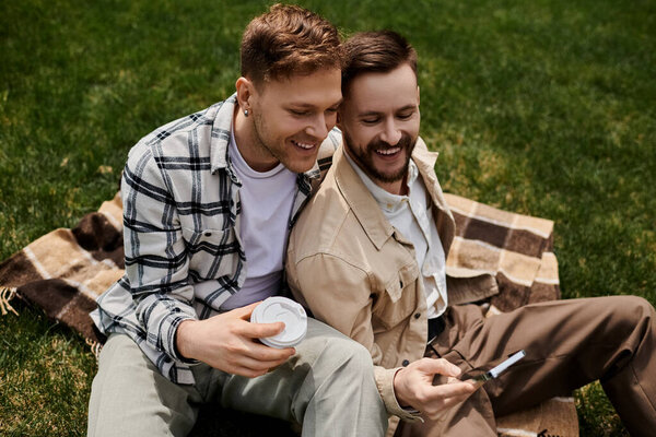 Two men in casual clothing sit peacefully atop a grassy field.