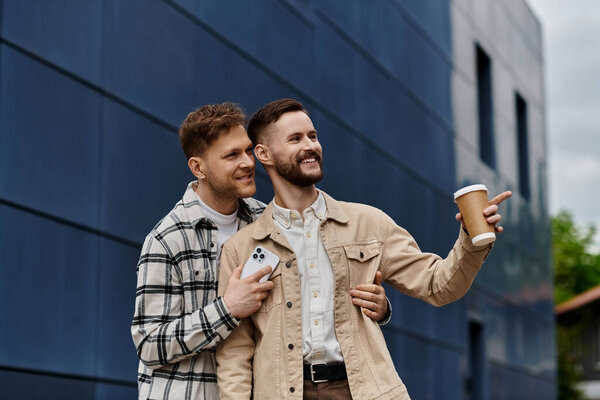 Двое мужчин в повседневной одежде, держат кофейные чашки на улице.