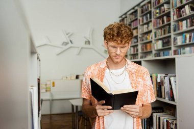 Kütüphanede kitap okumaya dalmış genç bir adam..