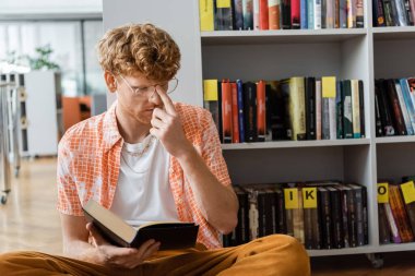 Young man immersed in book while seated on floor. clipart