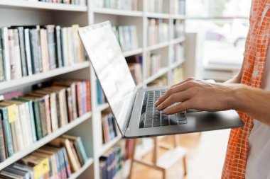 A student engrossed in studies, using a laptop in a library. clipart