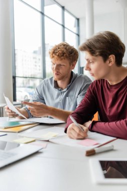 Two men deep in study, papers and pens scattered on the table. clipart