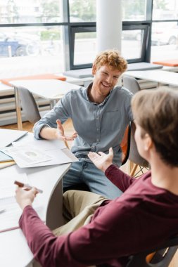 Two diligent male students engrossed in deep discussion at a library table. clipart