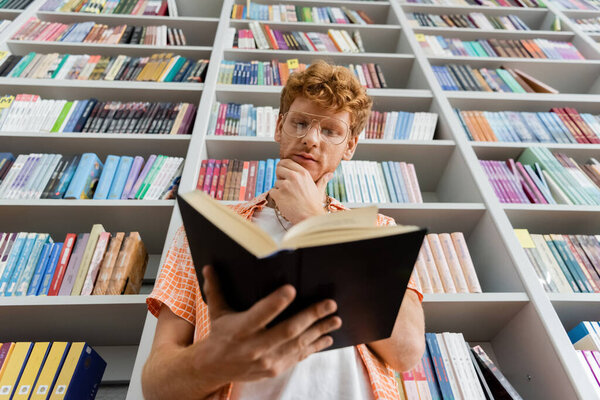 Young man engrossed in a book in a quiet library.