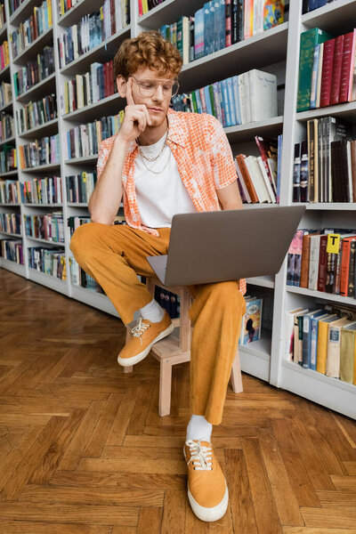 A man immersed in work on his laptop while sitting on a chair.