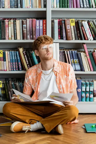 stock image A man sits on the floor in front of a bookshelf.