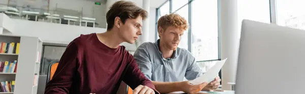 stock image Two men engrossed in studying together at a computer screen in a library.