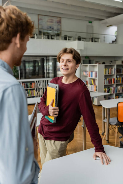 Мужчина стоит за столом в библиотеке рядом со своим другом.