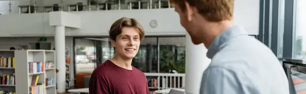 stock image Two young male students discussing amidst shelves of books.