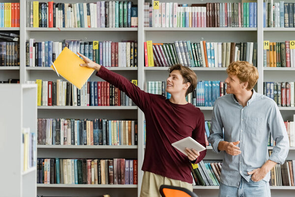 Two male students peruse a vast bookshelf in a scholarly setting.