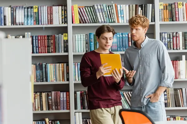 stock image Two male students immerse in the world of books at a bookshelf.