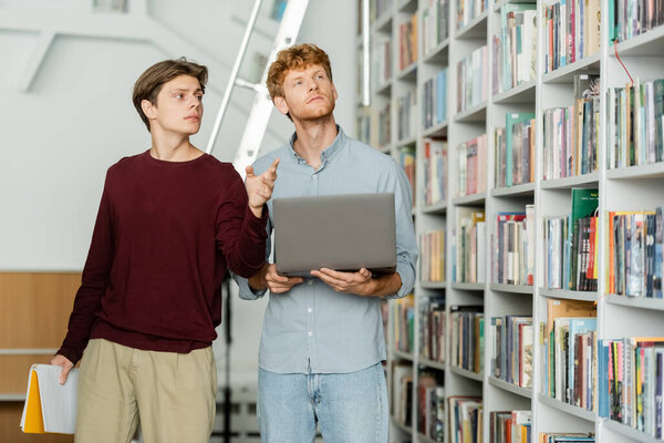 Двое мужчин, занятых исследованием ноутбуков, среди стопок книг в библиотеке.