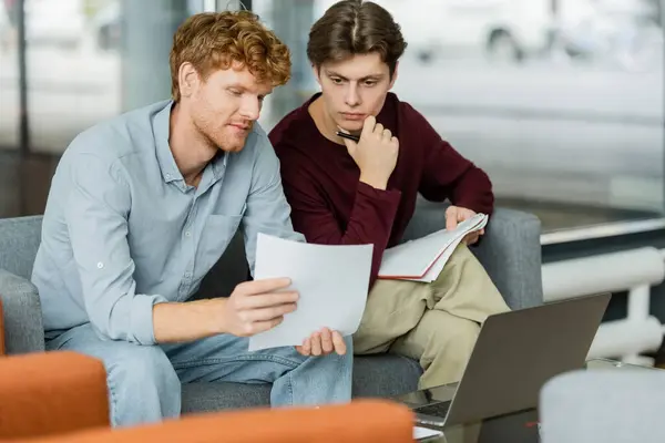 stock image Two men focus on a paper while sitting on a couch.