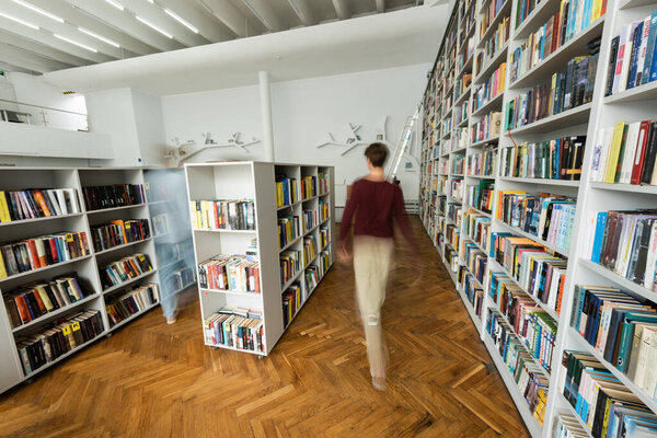 Two male students strolling through a vast library brimming with books.